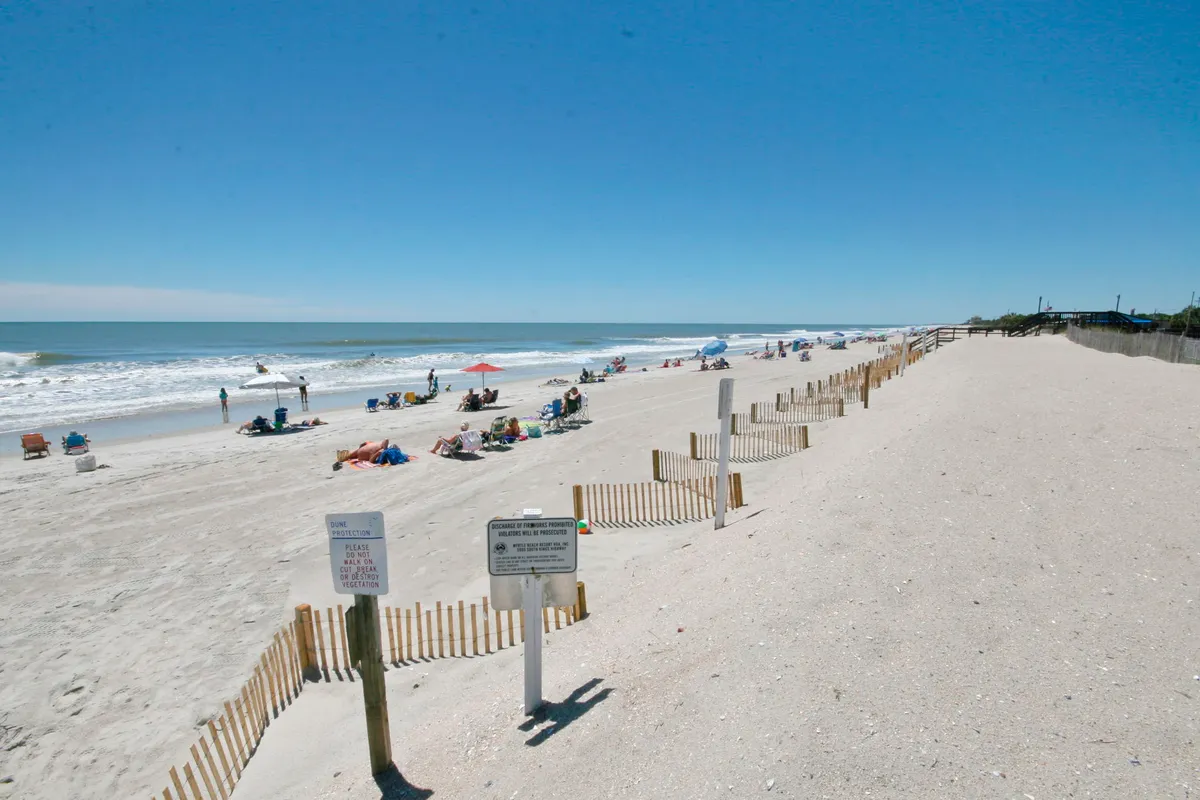 A picture of the sandy Myrtle Beach shoreline, featuring beach chairs and umbrellas set out along the sand, gentle ocean waves rolling in, and fences marking off areas. The mood is leisurely and inviting, perfect for a romantic stroll or soaking in the view.