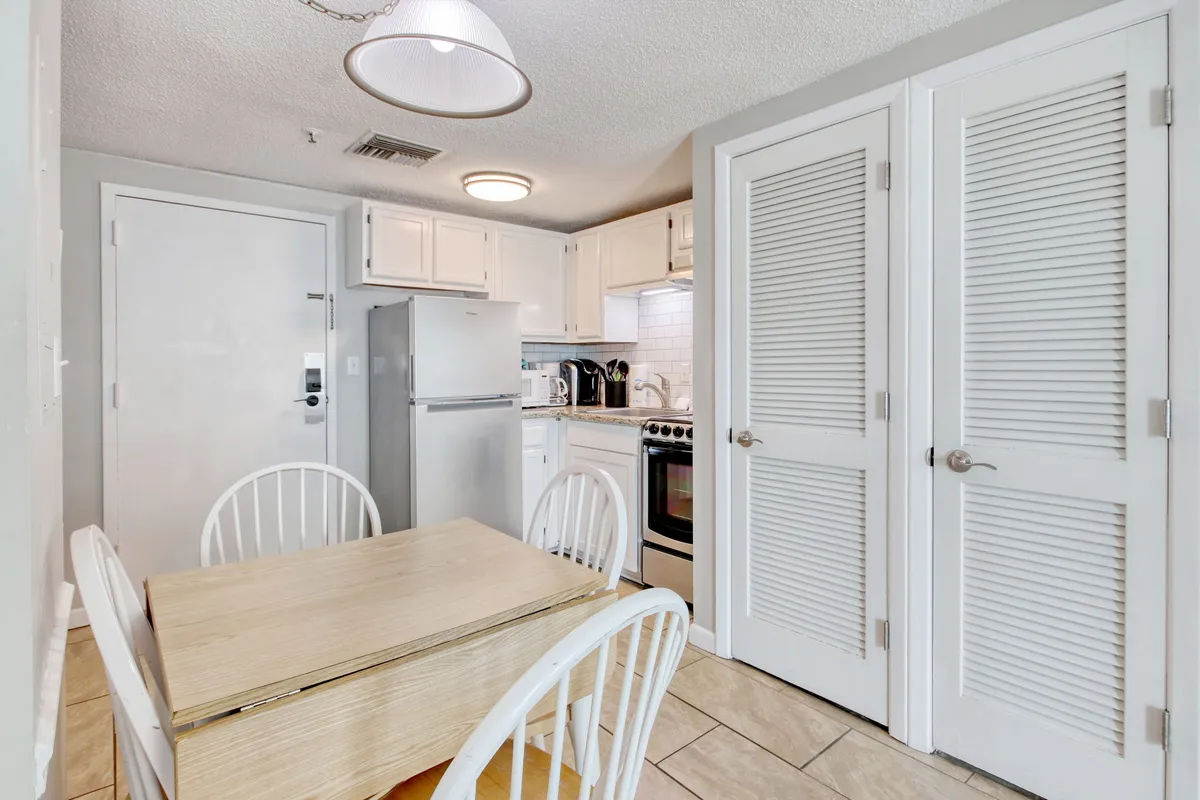 An inviting dining space adjacent to the kitchen, featuring a cozy dining table surrounded by kitchen appliances and white cabinetry. The scene feels homey and functional, hinting at the ease of transitioning from meal prep to dining in a comfortable setting.